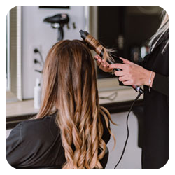 Photo d'une cliente qui se fait boucler les cheveux dans un salon de coiffure